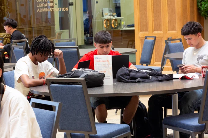 [ID: Pictured is a photo of three students sitting at a table on the sixth floor of the UTA Central Library studying.]
