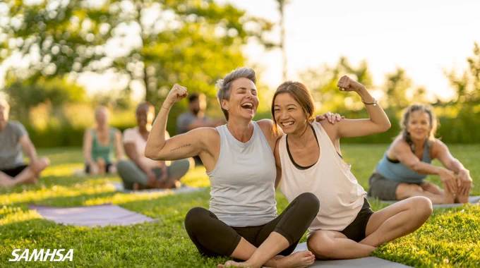 Mother and daughter joyfully interacting during a yoga class in a sunny park, with other participants in the background. Image includes SAMHSA logo.