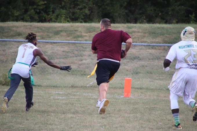 A player reaches forward to grab the flag off another player's belt from a differnt team. 
