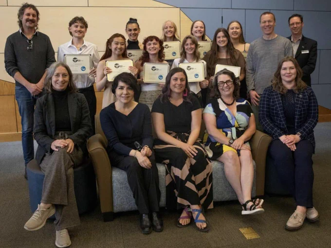 Group of individuals holding certificates, smiling in a seminar room.