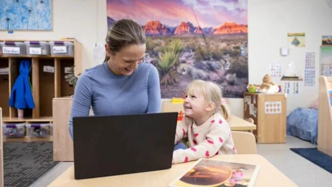 Mother working on her laptop during drop-off as her daughter tries to get her attention at a childcare center on a college campus.