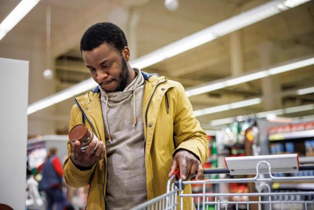 Person shopping in a supermarket, examining a product while pushing a shopping cart.
