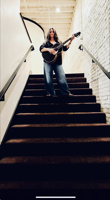 Diana standing on back staircase, posing with guitar, backstage Antone’s