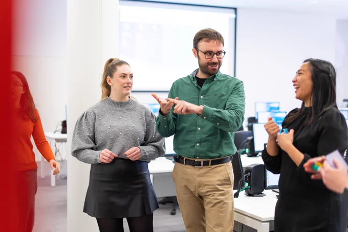 Decorative image that shows employees at EMBL-EBI stand in the training suites smiling and networking at a bioinformatics training course.