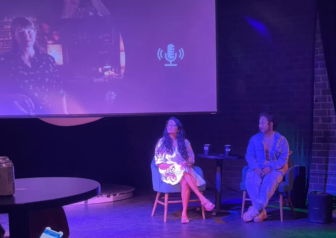 Tiffany and CoCo seated on stage at a during Q&A at the event, with a projected image of Jessica who joined virtually on the screen behind them.