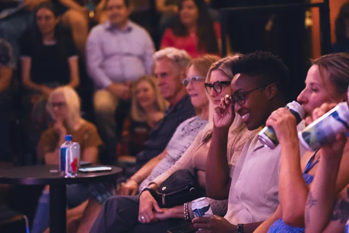 Audience members smiling and watching a performance at a venue.