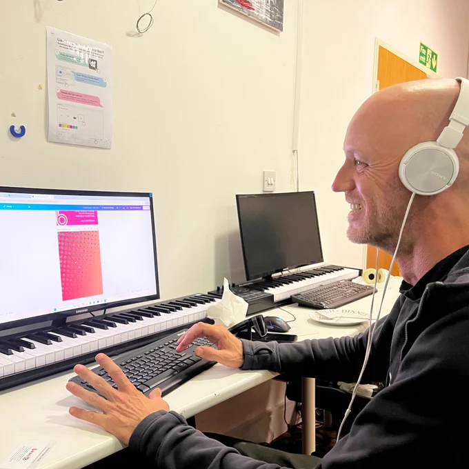An image of a staff member from Swansea Community Workshops sitting and smiling whilst working at a computer desk and typing on a keyboard.