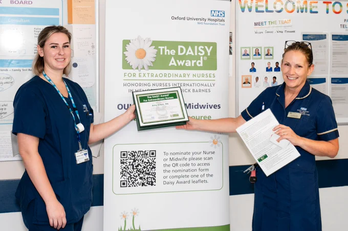 Amy Clark, our 50th DAISY Awardee, receiving the award from Lisa Butcher, Divisional Director of Nursing SUWON Division, standing in front of a DAISY Award display banner.