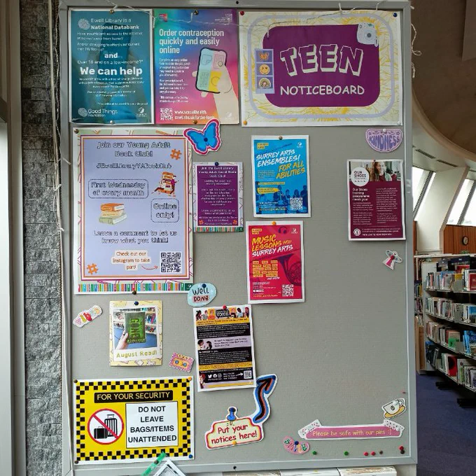 Photograph of a grey noticeboard with a poster saying "Teen Noticeboard" in a purple box against a yellow sunflower background pinned in the top right corner. Other signs include, leaflets promoting youth services, a poster promoting the Ewell Library Young Adult Book Club, and a yellow security notice saying "Do not leave bags/items unattended".