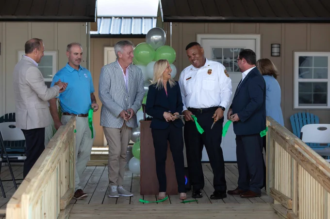 a group of seven people smiling after cutting a green ribbon opening the Tiny Home Village at the Sulzbacher Center