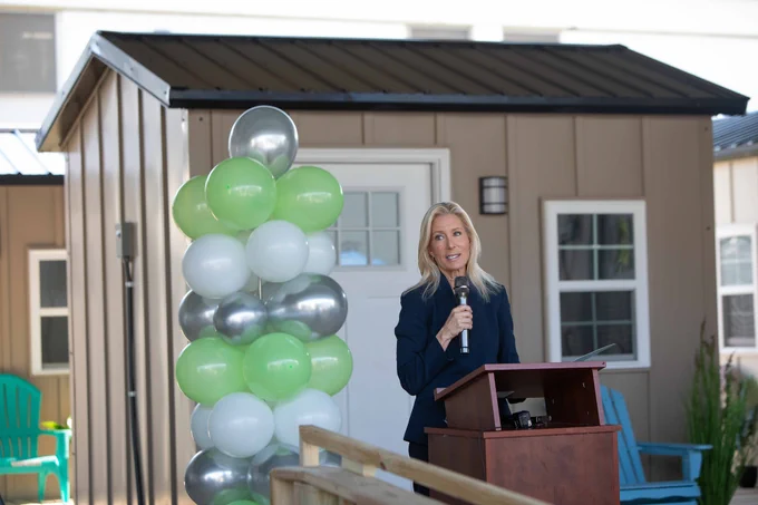 Mayor deegan speaking into a microphone with green, white, and silver balloons next to her