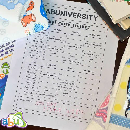 A paper class schedule is laid on a table surrounded by diapers, books, and a certificate. The schedule lists "Diaper Changing 101", "ABC and More 201", and other ageplay geared topics. At the bottom in red reds "10 off storewide!"