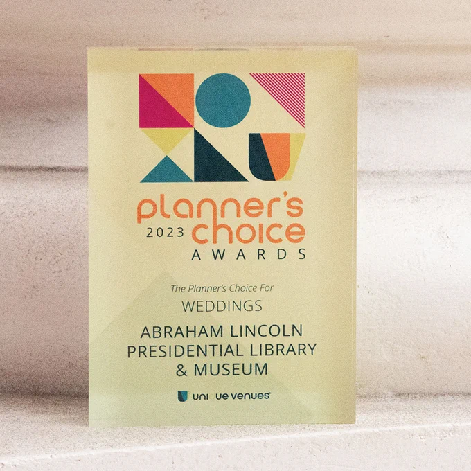 A glass award plaque with colorful geometric shapes reads: “2023 Planner’s Choice Awards – The Planner’s Choice for Weddings – Abraham Lincoln Presidential Library & Museum.”