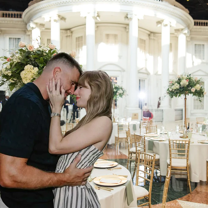 An edited photo of Taylor Swift and Travis Kelce embracing is placed in front of a wedding reception setup inside the Abraham Lincoln Presidential Museum plaza, with elegant tables, gold chairs, and tall floral arrangements.