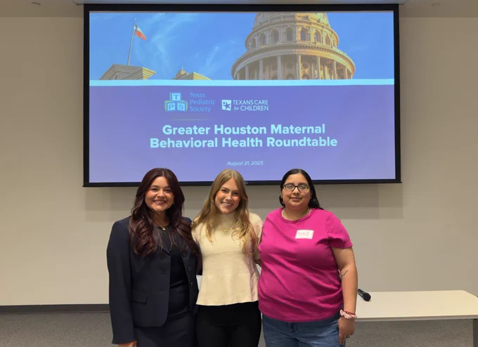Picture of three women smiling at the camera in front of a screen with a slide saying "Greater Houston Maternal Behavioral Health Roundtable."