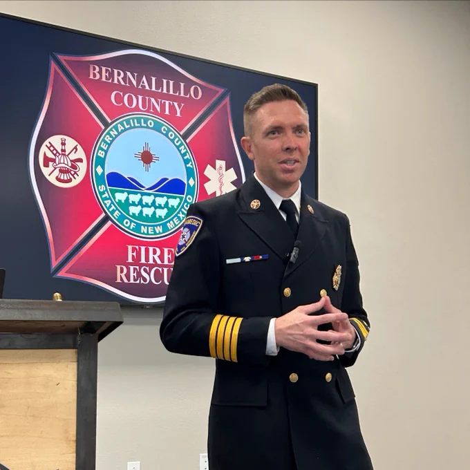 Deputy Fire Chief Zachary Lardy standing in uniform next to the Bernalillo County Fire & Rescue insignia.