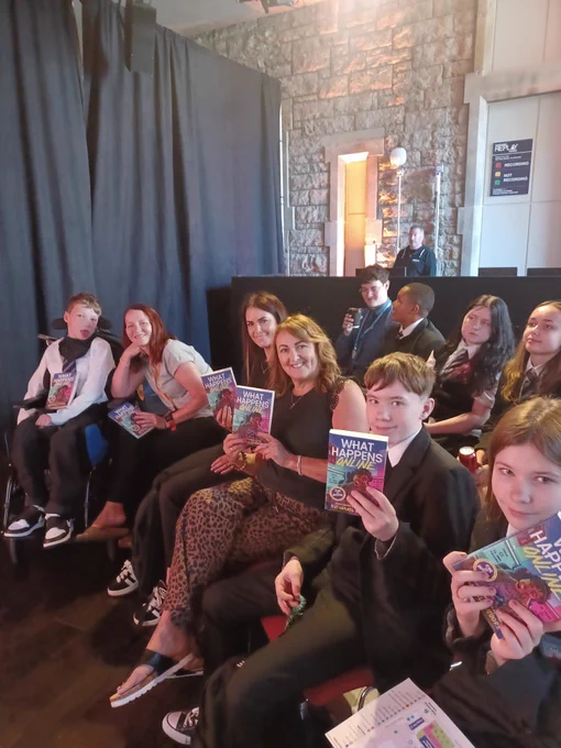 A row of pupils holding up Nathaneal Lessore's book "What Happens Online."