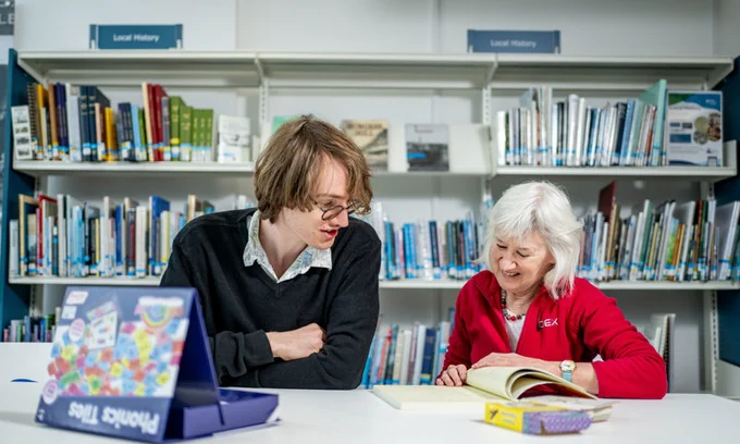 Young man and lady sitting down together at a desk in a library