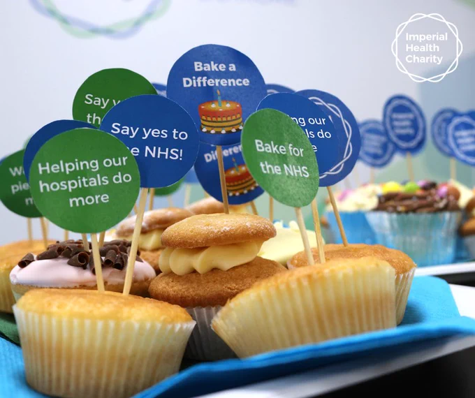 Close-up of cupcakes with blue and green signs promoting NHS support and baking for charity on a blue napkin.