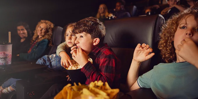 Audience of various ages enjoying a film in a movie theater, with focus on a child eating popcorn.
