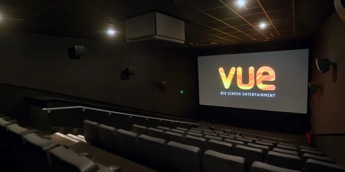 Interior view of a Vue cinema theater showing empty seats and a brightly lit screen displaying the Vue logo.