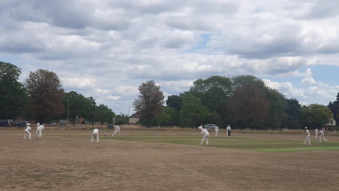 View from boundary shows slip, gully and other fielders watching on as batter tries to hit ball as umpire looks on