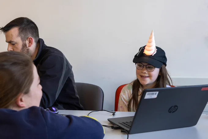 A young girl smiles while wearing a hat with a lit up unicorn horn on it.