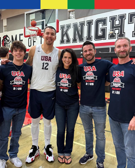 Group photo with a basketball player in a USA jersey numbered 12 and four fans wearing USA Basketball shirts, standing in a gym under a basketball hoop.