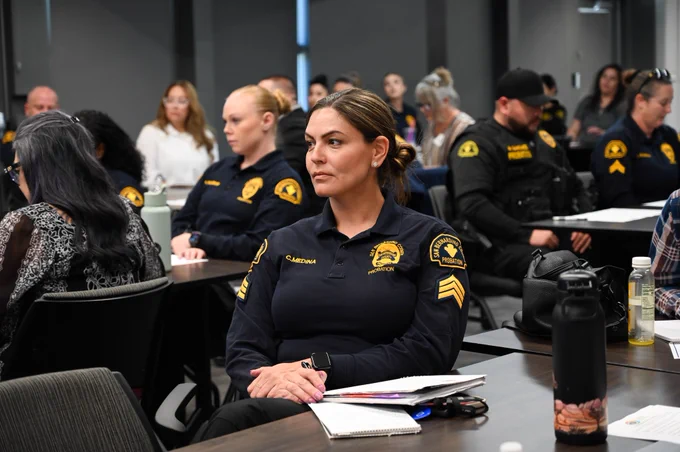A female officer listens attentively during a group session, with other attendees visible in the background.