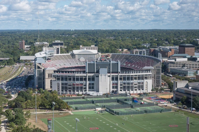 Aerial view of Ohio Stadium, home of the Ohio State Buckeyes, on a sunny day with surrounding green areas and parking.