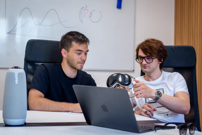 Two young engineers sit at a table in front of a laptop. Cornel Amariei hands an Apple Pro Vision headset to intern Vlad Marian, while both review something on-screen.  The scene captures a hands-on design session between mentor and mentee, highlighting innovation, collaboration, and emerging tech talent.​ 

ext on the image:​

We love seeing young talent soar at @dotlumen. ​

Earlier this summer, we opened one internship position. ​

Out of 1,000 candidates, we picked Vlad, a brilliant Gen-Z .​

Now he's in Australia, piloting a solar vehicle with a UTCN project.