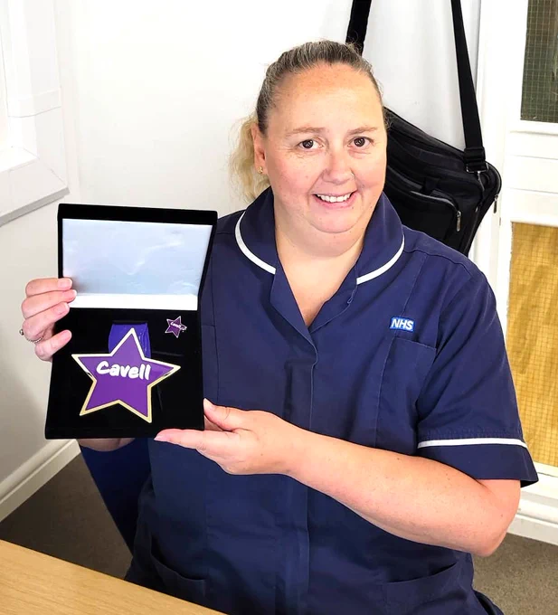 Photo of nurse holding her Cavell Star award. Dark blue uniform, hair tied back.