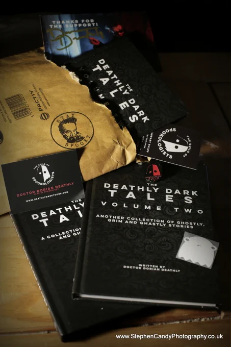 Copies of the book "The Deathly Dark Tales Volume Two" spilling out of the envelope they arrived in, along with Spookologist bookmarks, a pin badge, a Nope ghost sticker and a signed postcard.