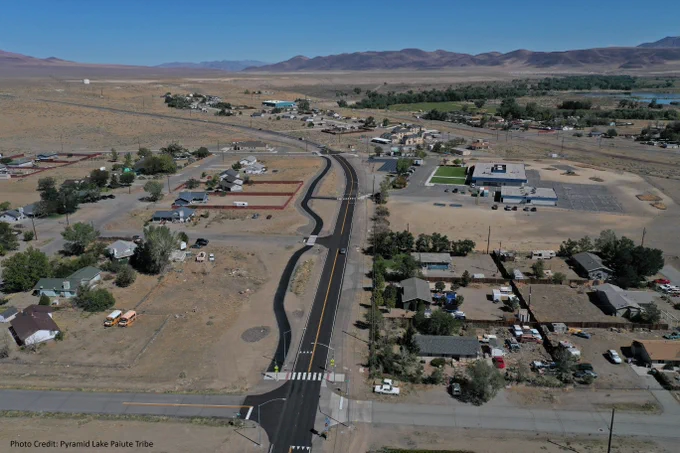 Aerial view of a small town with roads, buildings, and distant hills, near Pyramid Lake.  A pedestrian/bike is seen parallel to the main road with a well-marked crosswalk.
