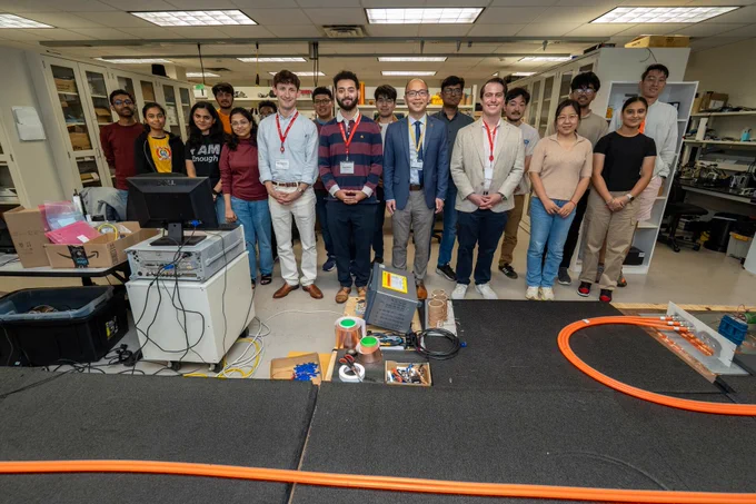 A large group of people posing for a photo in a robotics lab with equipment in front of them.