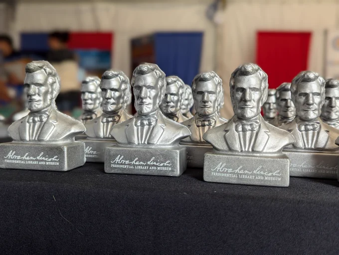 Rows of small silver Abraham Lincoln busts sit on a black tablecloth at the ALPLM booth inside the Governor’s Tent at the DuQuoin State Fair.