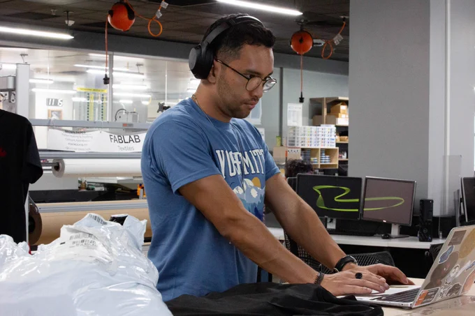 [ID: Pictured is a photo of a student working on a laptop computer in the FabLab on the first floor of the UTA Central Library.]