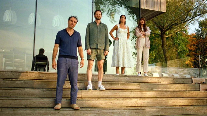From L to R, Michael Angelo Covino, Kyle Marvin, Adria Arjona, and Dakota Johnson stand outside of a swanky house looking perplexed at something happening out of frame in a still from the film SPLITSVILLE. 