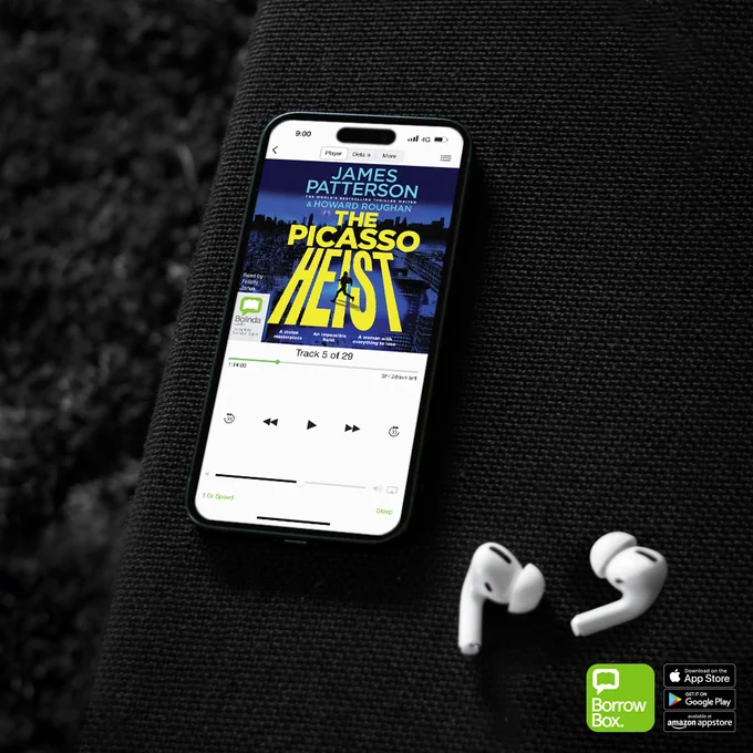 Smartphone displaying audiobook 'The Picasso Heist' by James Patterson playing on a dark fabric surface next to white wireless earbuds.