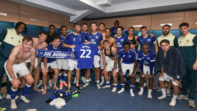The squad hold up a Cardiff City shirt with 'Bamba 22' printed on the back.