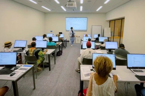 A classroom setting with multiple attendees using computers and focusing on a presentation being given by a facilitator at the front near a digital whiteboard.