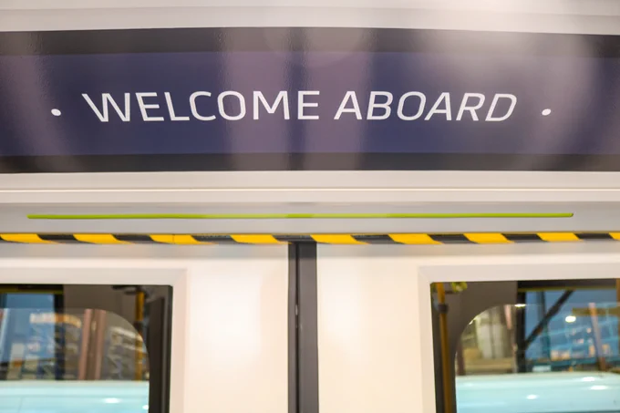 Close-up of a train door with a blue sign above reading 'WELCOME ABOARD' in white letters.