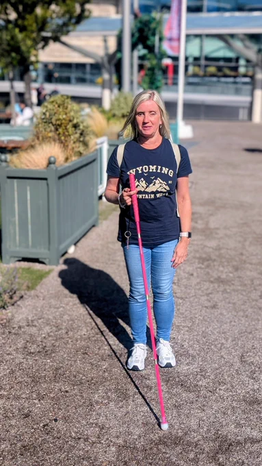 Woman walking outdoors in Liverpool with a bright pink cane.
