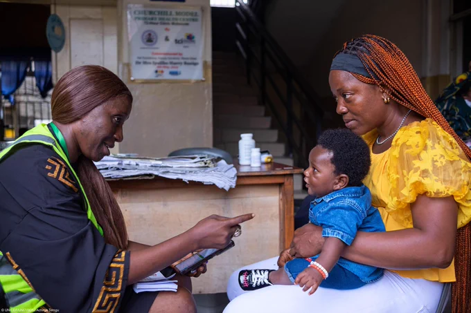 Photo of an Adhoc Registrar, supports a mother during a digital birth registration drive in Port Harcourt, Nigeria, part of a nationwide effort to ensure every child has a legal identity.  © UNICEF 2024