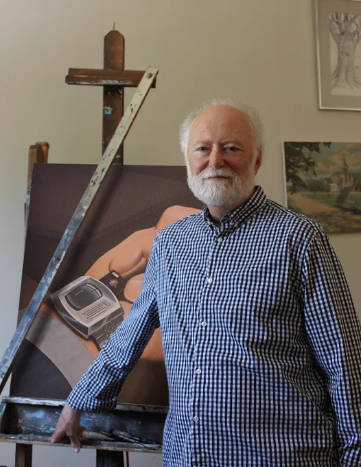 A white-bearded Robert Tinney stands near an easel with a famous Tinney illustration of a smartwatch that runs on a micro-floppy disk.