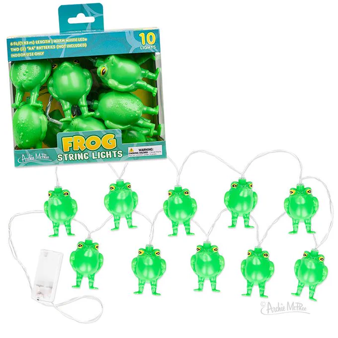 Frog String Lights product shot with the retail box and all ten frogs spread out along the wire. Box is teal and green with a window showing the frogs packed inside. Specs on the package: 6 feet long, warm white LEDs, two AA batteries not included, indoor use only. Battery pack visible at one end. Each frog stands upright with that same pot-bellied, slightly confused posture that makes them weirdly endearing even when they're off.