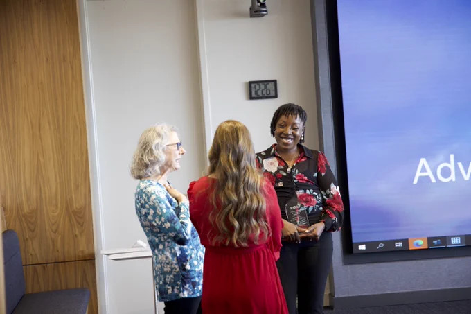 Three people are standing in a room having a conversation. One person is holding a glass award.