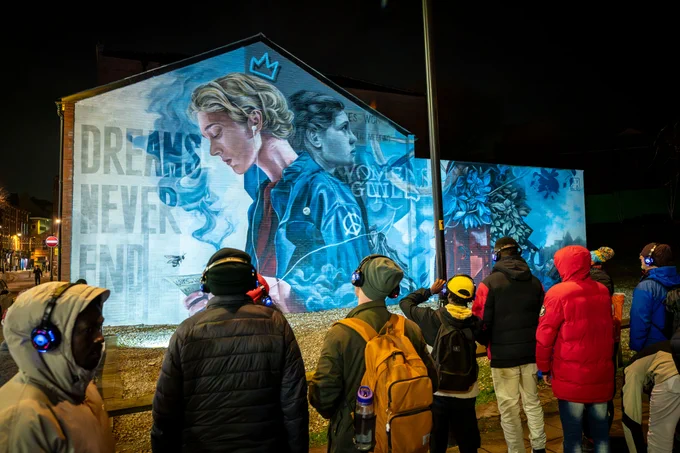 Crowd looking at a mural of a woman