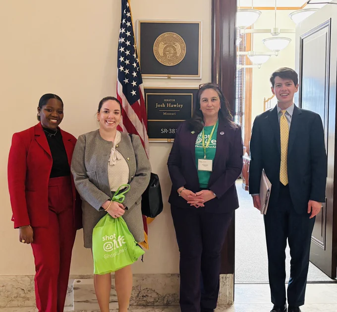 Four people beside flags in front of Senator Hawley’s office in Washington DC With a green Shot@Life bag