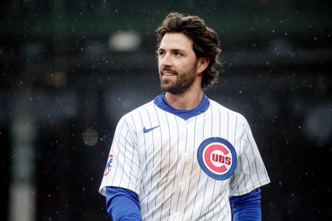 Candid photo of Dansby Swanson in a Cubs home uniform with warm layers underneath and precipitation falling around him.